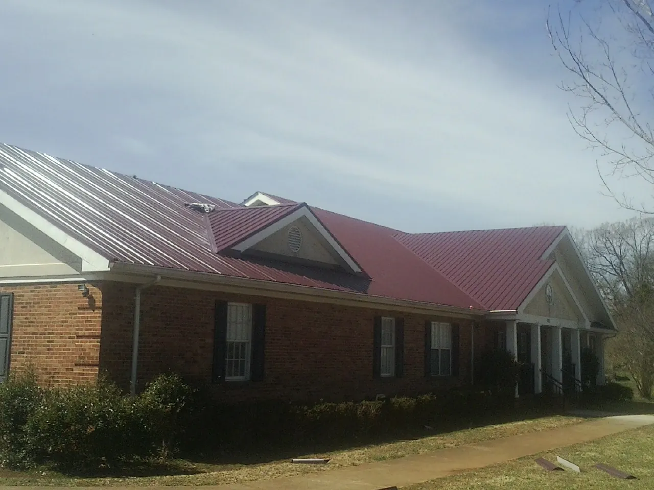 Red metal roof with gabled entries on a long brick building, from a Hail Damage Roof Repair job in Allentown