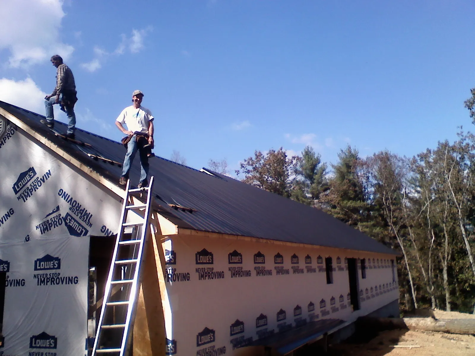 Two roofers standing on a long dark metal roof over a wrapped building in Allentown